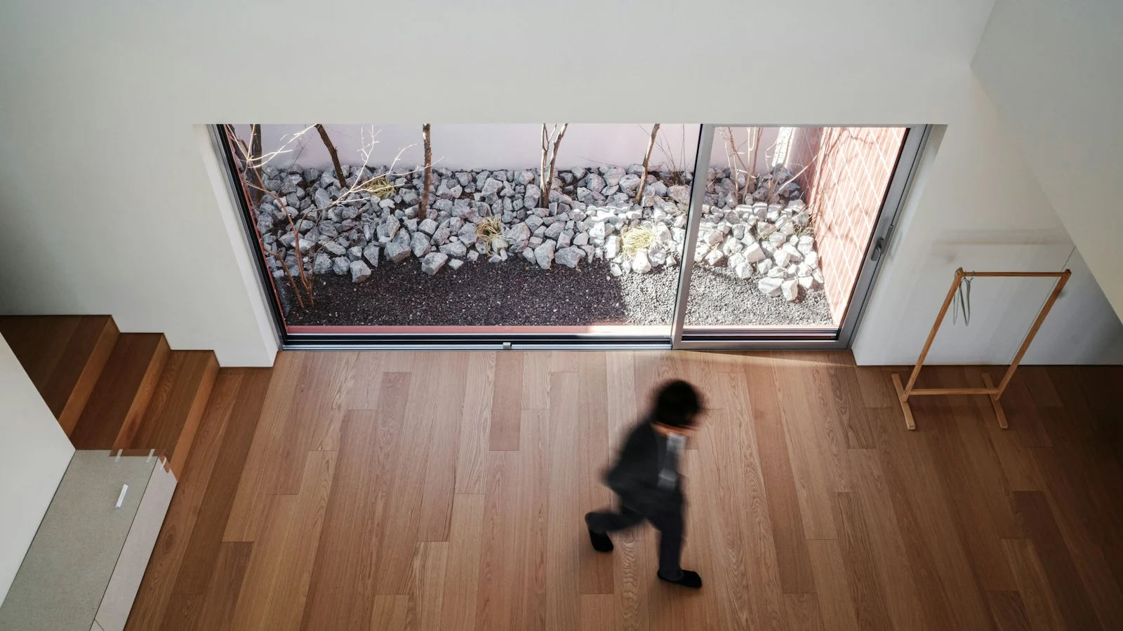 A child moves across a wooden floor near a large window, photographed from above
